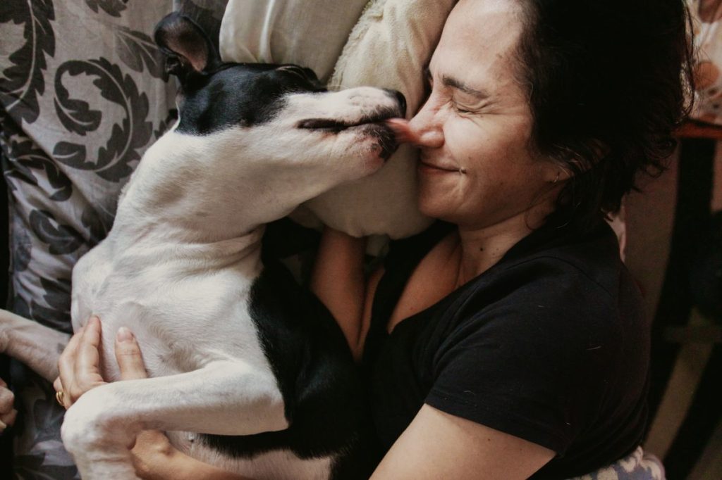 Dog licking woman’s face in bed.